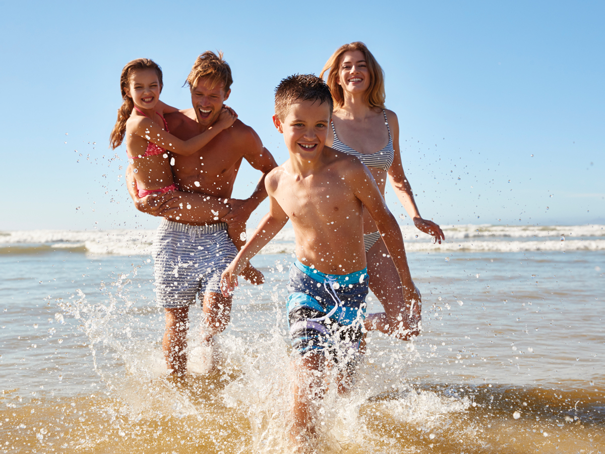 Happy family in bathing suits walking along beach smiling