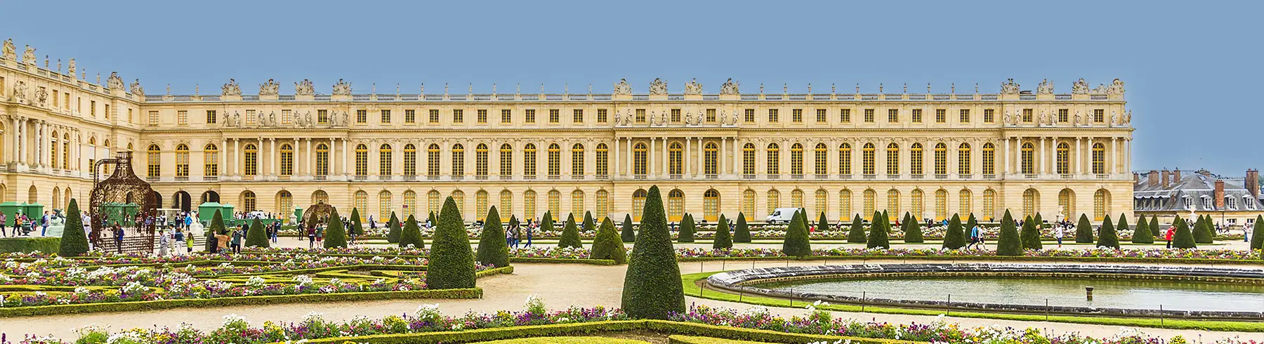 A panoramic view of the gardens at the Palace of Versailles, showcasing manicured hedges and vibrant flower beds.